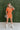 Frontal view of the Spur The Moment Denim Romper that features an orange denim material, a surplice neckline that snaps with a collar, half-length sleeves, a front zipper, pockets, pleating on the legs, and a 3" inseam.