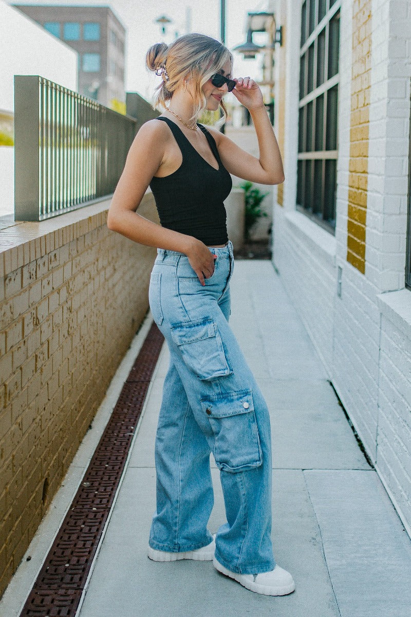Side view of model wearing the Dakota Cargo Jeans that have blue denim fabric, pockets, a front zipper with a button closure, belt loops and wide legs