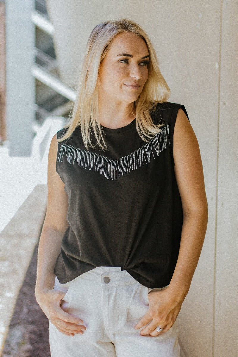 Front view of model wearing the I'm All In Fringe Top that has black knit fabric, a silver beaded fringe design, a round neckline and a sleeveless design