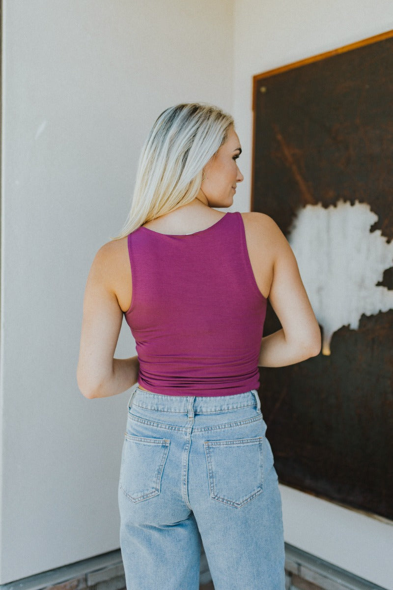 Back view of model wearing the Here We Go Tank Top that has purple knit fabric, a round neckline and a sleeveless design.