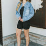 Full body front view of model wearing the Over it Cropped Denim Jacket that has blue denim fabric, a cropped waist with a raw hem, a button up front, pockets, a collared neck, and long sleeves.
