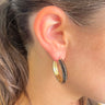 Close up view of model wearing the Blindsided Hoop Earrings which features medium, closed hoops with gold and black color-block design.