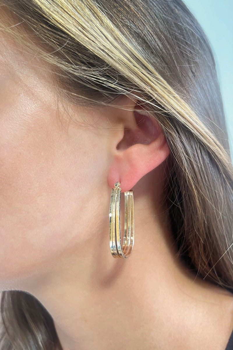 Side view of model wearing the Cheap Thrills Earrings which features scooped, closed hoops with gold lines design.