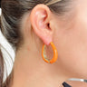 Side view of model wearing the Around The Block Earrings in Orange which features medium, closed orange hoops with gold details.