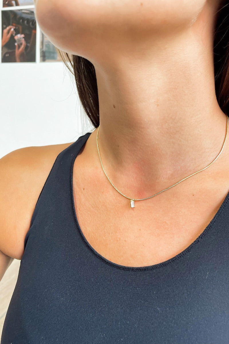Front view of model wearing the Simple Is Best Necklace which features flat gold necklace with a rectangle shaped clear stone.