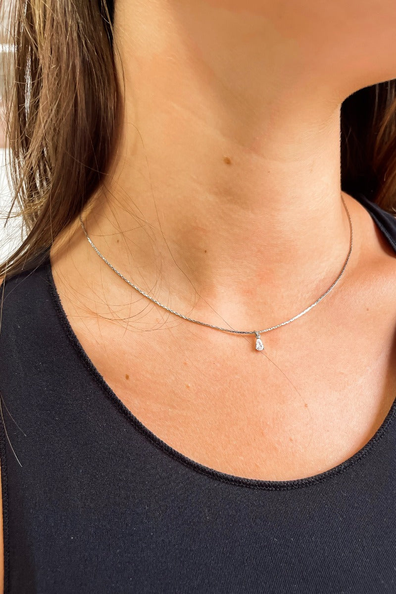 Close up view of model wearing the All For You Necklace which features silver flat necklace with a teardrop shaped clear stone.
