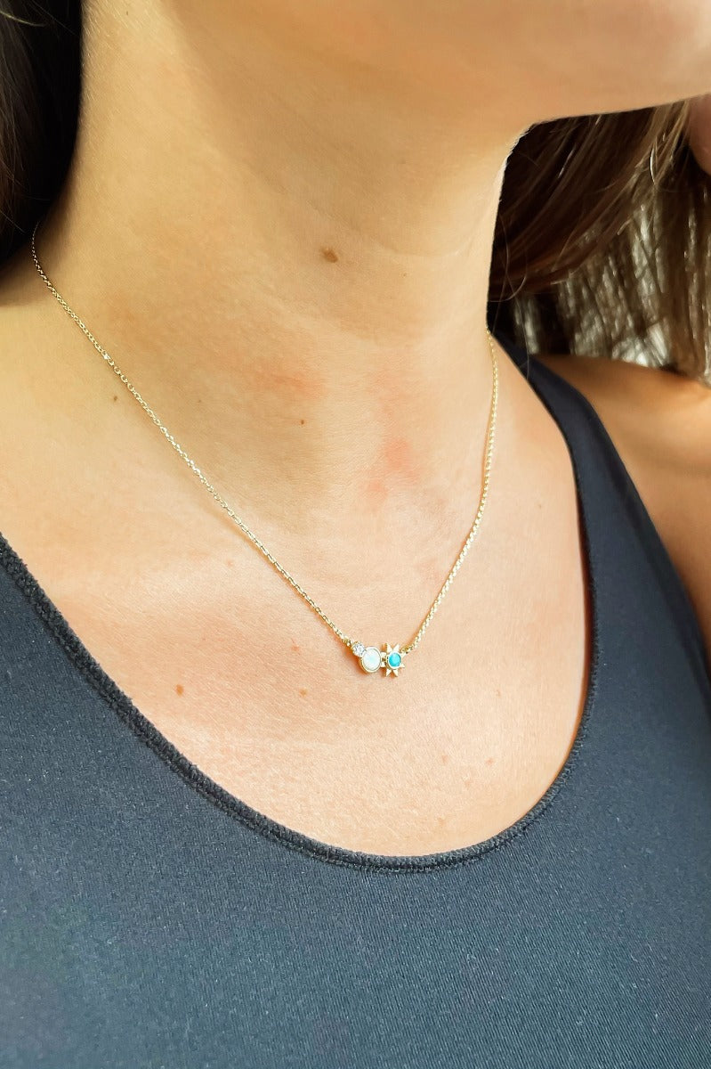 Close up view of model wearing the Starburst Necklace in Turquoise which features gold chain link with clear stone, opal stone and turquoise sun medallion.