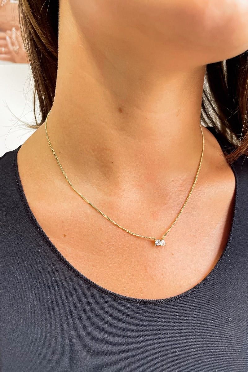 Front view of model wearing the Connected By Our Hearts Necklace which features gold chain link with two clear stones paired together.