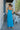 Full body back view of model wearing the Coastal Paradise Dress that has cobalt blue ribbed fabric, midi length, a round neckline, an elastic waistband, and spaghetti straps