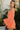 Side view of model wearing the Take Me To The Tropics Romper that has coral fabric, an elastic waist, a tie around the waist, an off-the-shoulder neck, and 3/4 flare sleeves with ruffle trim.