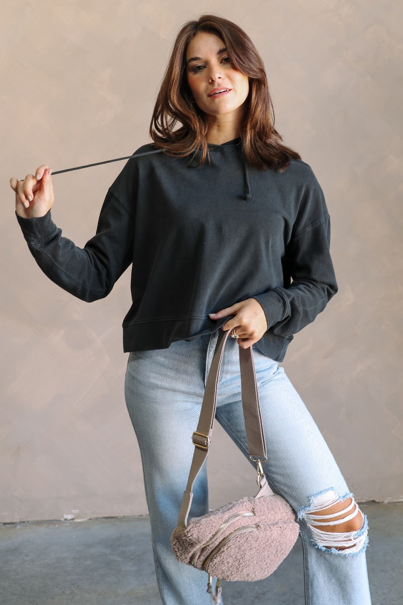 Front view of model wearing the Chloe Black Hoodie Long Sleeve Sweatshirt which features washed black cotton fabric, a thick hem, a high neckline with a hood attached and drawstring ties, dropped shoulders, and long sleeves with cuffs.