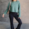 Full body front view of model wearing the Nicole Green Cropped Long Sleeve Sweatshirt that has gray-green cotton fabric, a cropped waist, a round neckline and long sleeves.