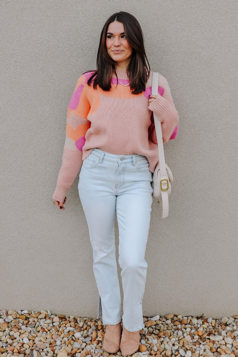 Full body view of model wearing the Mila Pink Multi Long Sleeve Sweater which features orange, peach, cream and fuschia knit fabric, an upper floral print, ribbed hem, a ribbed round neckline, dropped shoulders, and long sleeves with ribbed cuffs.