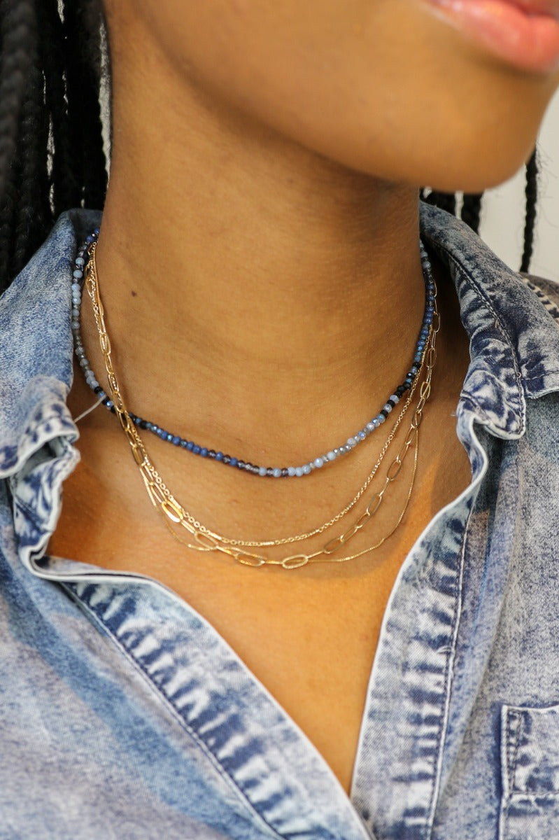Close front view of model wearing the Gianna Blue and Gold Layered Necklace that feautures 4 layers: 3 varied gold chains and one blue beaded strand.