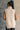 Back view of model wearing the Olivia Beige Cable Knit Turtleneck Sleeveless Sweater which features beige cable knit fabric, high low hem, turtleneck neckline and sleeveless.
