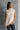 Front view of model wearing the Olivia Beige Cable Knit Turtleneck Sleeveless Sweater which features beige cable knit fabric, high low hem, turtleneck neckline and sleeveless.