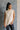 Front view of model wearing the Olivia Beige Cable Knit Turtleneck Sleeveless Sweater which features beige cable knit fabric, high low hem, turtleneck neckline and sleeveless.