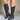 Side view of model wearing the Arcadia Black Western Boots that feature black faux leather, cream western stitching, and black soles with 3 inch heels.