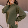 Front view of model wearing the Aria Olive Green Pattern Lounge Top which features olive green knit fabric, a monochrome geometric quilted pattern, a round neckline, and long balloon sleeves with cuffs.