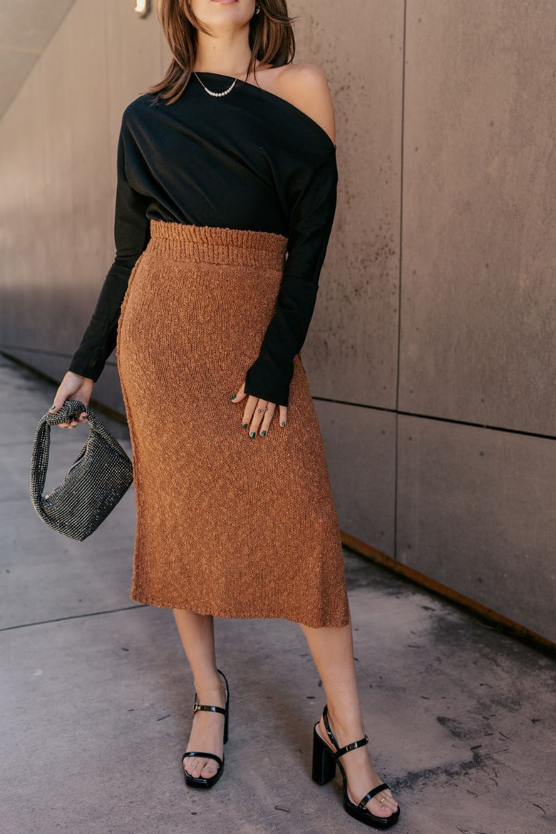 Front view of model wearing the Audrey Light Brown Textured Midi Skirt which features light brown textured knit fabric, midi length, a slit on the side, light brown thigh length lining, and an elastic waistband.