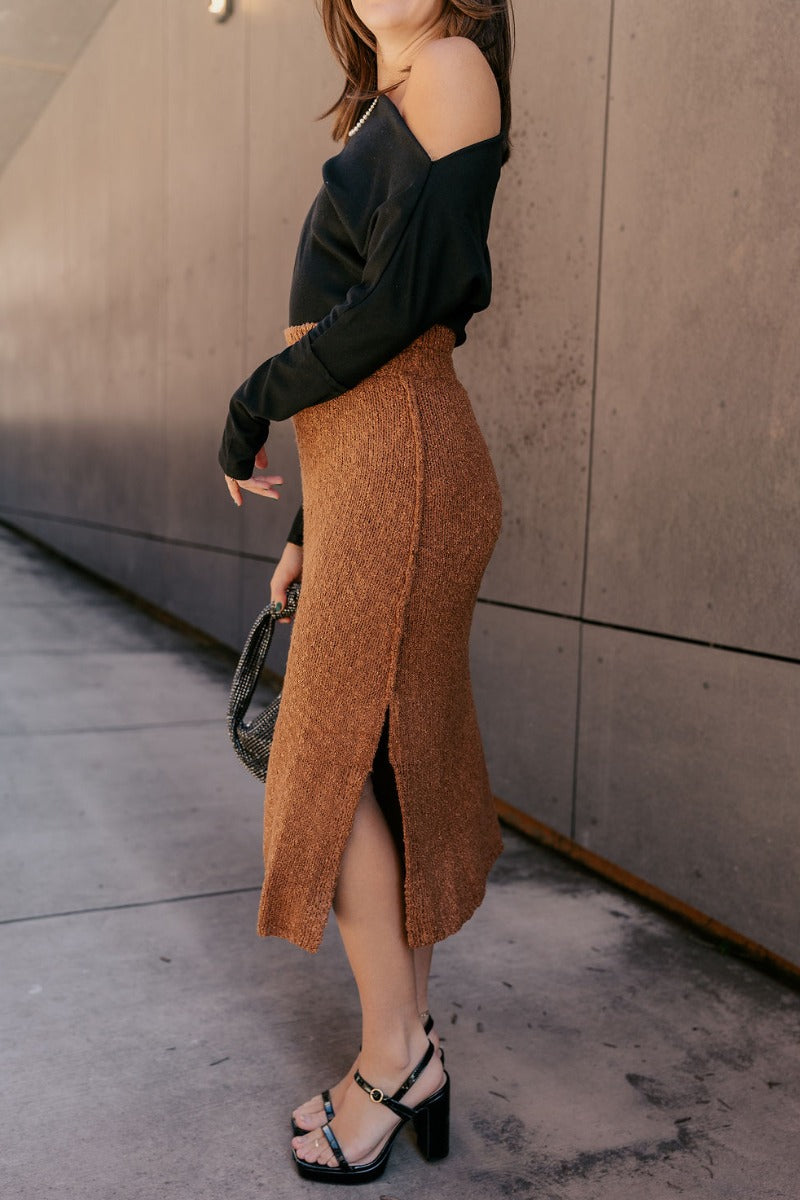 Side view of model wearing the Audrey Light Brown Textured Midi Skirt which features light brown textured knit fabric, midi length, a slit on the side, light brown thigh length lining, and an elastic waistband.