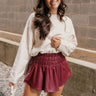 Front view of model wearing the Aurora Burgundy Faux Leather Ruffle Skort which features burgundy faux leather fabric, shorts lining, ruffle skirt detail, and a smocked elastic high waistband.