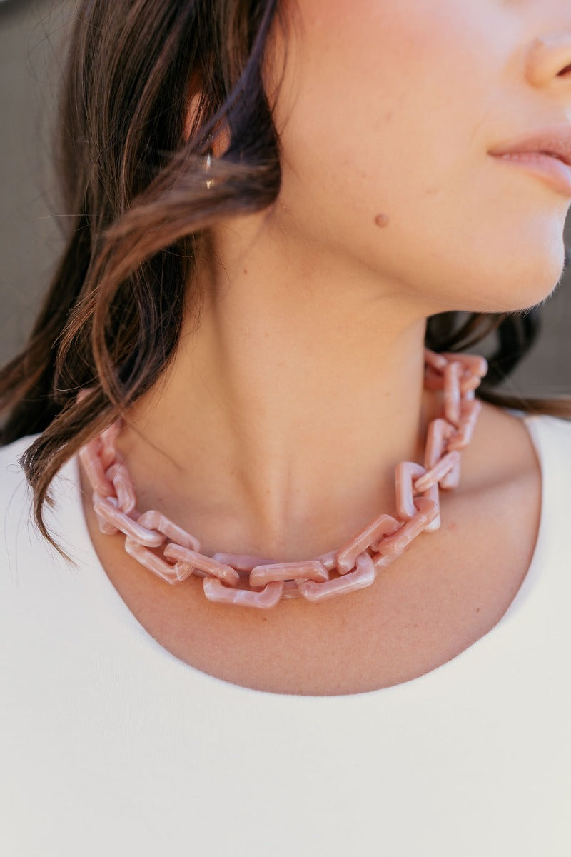 Close up of model wearing the Kendall Pink Chain Link Statement Necklace that has square shaped links with a blush and mauve marble design and a gold adjustable link closure.