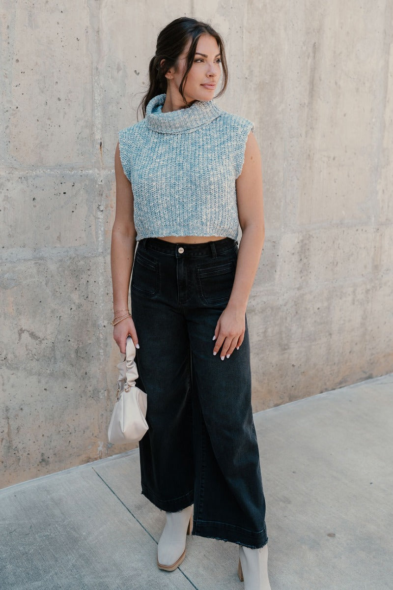 Full body view of model wearing the Jordyn Blue & White Sleeveless Turtleneck Sweater which features blue and white cable knit fabric, a cropped waist, a turtleneck neckline, and a sleeveless design.