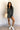 Full body front view of model wearing the Ezra Grey Green Long Sleeve Romper that has grey green knit fabric, pockets, an elastic waist, a front zipper, a hood, a skirt with fitted shorts , and long sleeves.