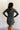 Back view of model wearing the Ezra Grey Green Long Sleeve Romper that has grey green knit fabric, pockets, an elastic waist, a front zipper, a hood, a skirt with fitted shorts , and long sleeves.