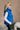 Side view of model wearing The Laurel Royal Blue Button-Up Puffer Vest features cobalt blue nylon puffer fabric, intertwined design, monochrome button up closure, high neckline and sleeveless.