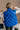 Back view of model wearing The Laurel Royal Blue Button-Up Puffer Vest features cobalt blue nylon puffer fabric, intertwined design, monochrome button up closure, high neckline and sleeveless.
