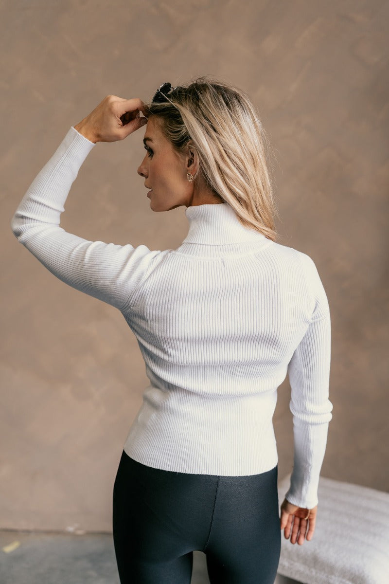 Back view of a model wearing The Elora Off White Long Sleeve Ribbed Turtleneck features off white ribbed fabric, turtleneck neckline and long sleeves.