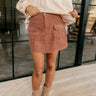 Front view of model wearing The Olivia Corduroy Cargo Skirt features light brick corduroy fabric, fray hem, mini length, two front crago pockets and front zipper with button closure.