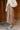 Side view of model wearing the Emmie Taupe Satin Pleated Midi Skirt that has taupe satin fabric, a plisse design, midi length, and an elastic waistband.
