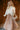 Front view of model wearing the Emmie Taupe Satin Pleated Midi Skirt that has taupe satin fabric, a plisse design, midi length, and an elastic waistband.