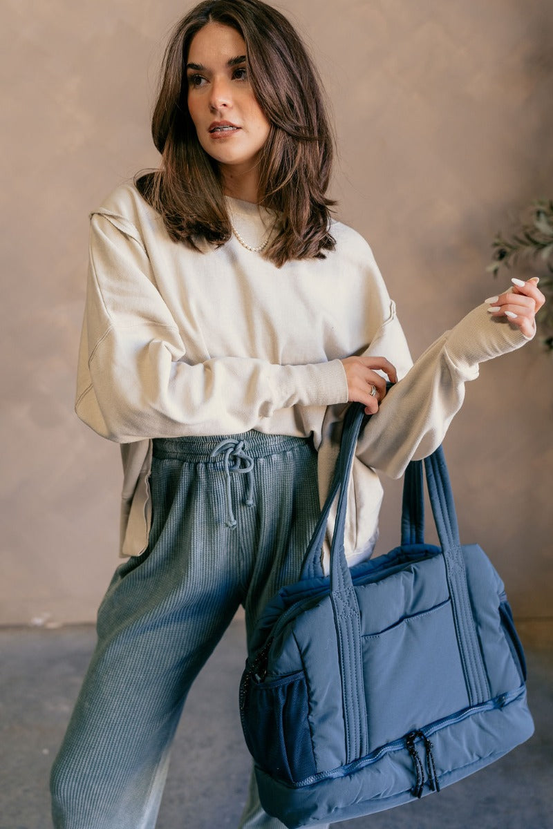 Front view of model wearing the Isla Blue Tote Bag which features teal lightweight fabric, quilted pattern, pockets on each side, inside divider with monochrome zipper and shoulder straps.