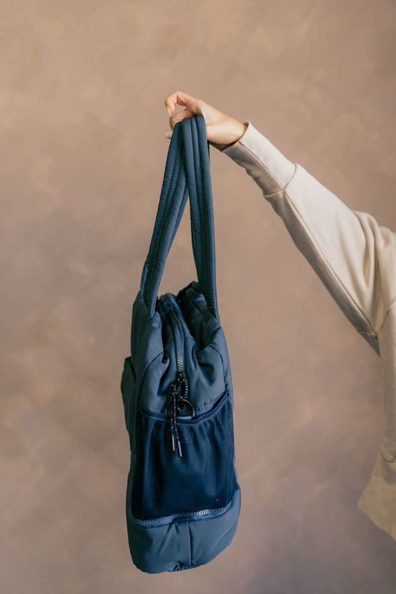 Side view of model holding the Isla Blue Tote Bag which features teal lightweight fabric, quilted pattern, pockets on each side, inside divider with monochrome zipper and shoulder straps.
