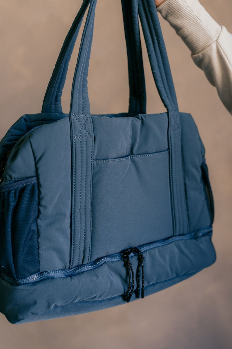 Close up view of model holding the Isla Blue Tote Bag which features teal lightweight fabric, quilted pattern, pockets on each side, inside divider with monochrome zipper and shoulder straps.