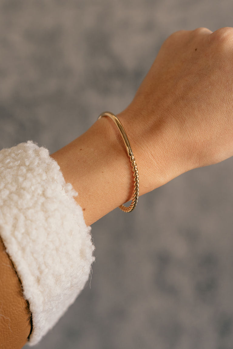Close up view of model wearing the Aria Gold Rope & Bar Bangle Bracelet which features gold bangle with roped details.