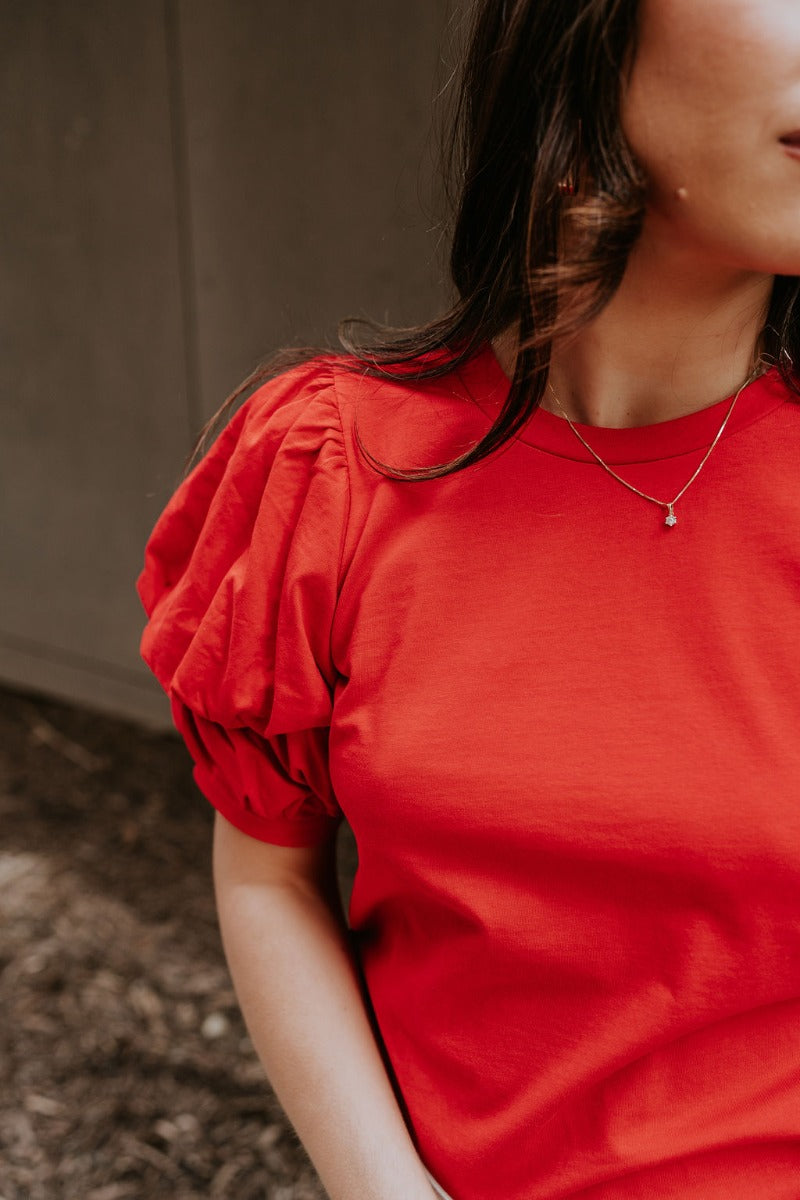 Close front view of model wearing the Maddie Red Puff Sleeve Top that features red cotton fabric, a round neckline, and short bubble puff sleeves.