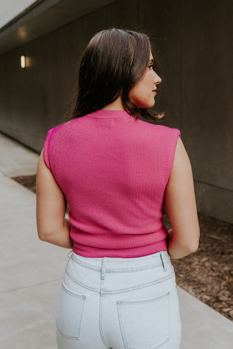 Back view of model wearing the Veronica Hot Pink Sleeveless Sweater that has hot pink knit fabric, a ribbed hem, a round neckline and a sleeveless design.