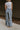 Back view of model wearing the Kelly Blue Wide Leg Drawstring Pants that have blue denim-washed light weight fabric, two front slit pockets, an elastic waistband with a drawstring tie, and wide pant legs.