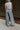 Back view of model wearing the Kelly Blue Wide Leg Drawstring Pants that have blue denim-washed light weight fabric, two front slit pockets, an elastic waistband with a drawstring tie, and wide pant legs.