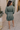 Back view of model wearing the Maya Olive Satin Ruffle Long Sleeve Dress which features olive grey satin fabric, mini length, ruffle details, a three-tier design, olive grey lining, a plunge neckline, long sleeves with elastic cuffs, and a back key hole w