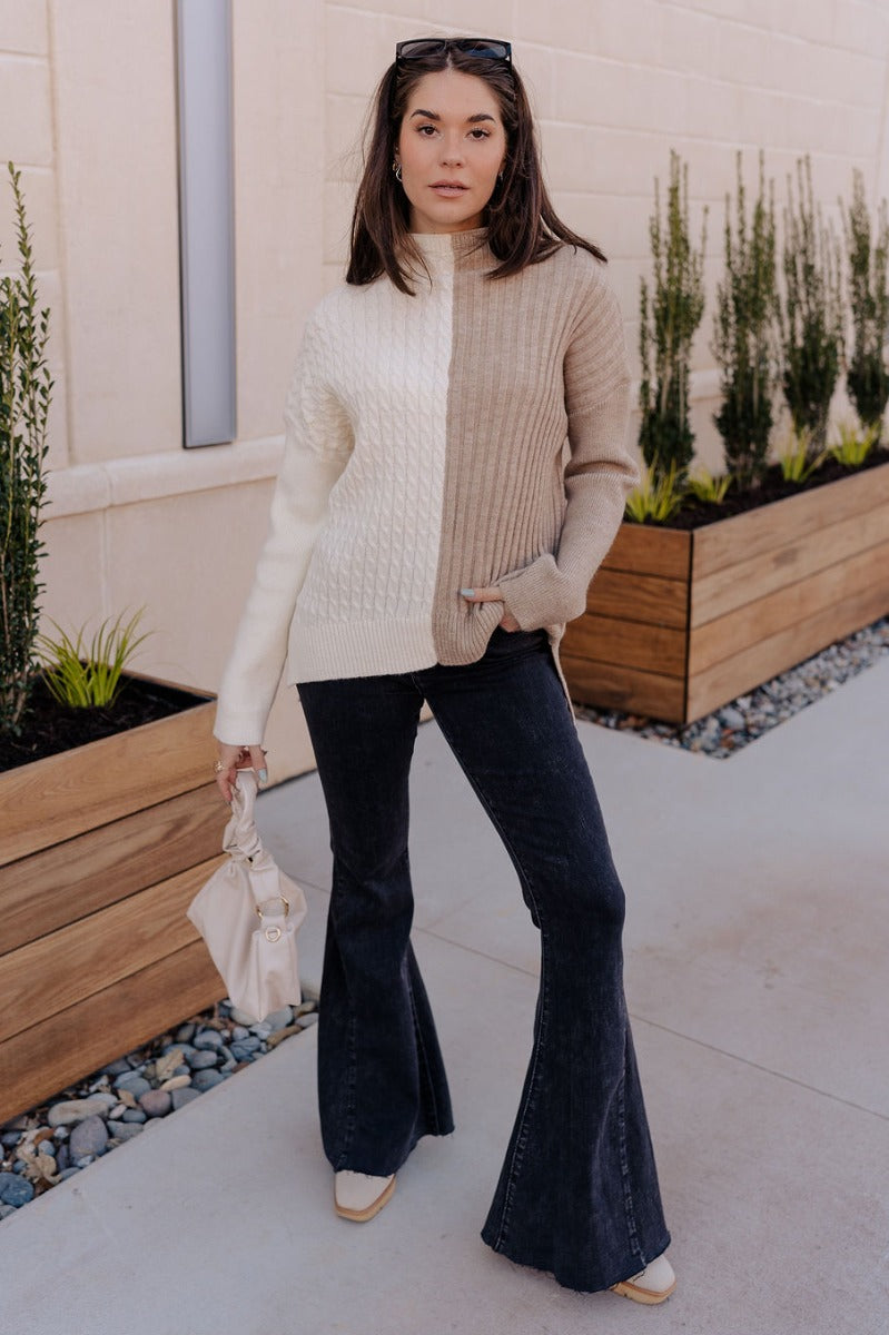 Full body view of model wearing the Lillian Taupe & Cream Long Sleeve Sweater which features cream cable knit fabric, taupe ribbed knit fabric, a color block pattern, a ribbed hem, slight slits on each side, a high neckline, and long sleeves with cuffs.