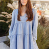 Front view of model wearing the Victoria Denim Babydoll Dress that has light washed denim fabric, a mini-length hem, tiered detailing, a v-neckline, and long balloon sleeves with elastic wrists.