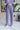 Front view of model wearing the Wanderlust Pants that feature purple plisse fabric, an elastic waistband, and wide legs with lettuce trim