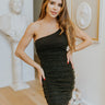 Front view of model wearing the Glam It Up Dress which features black sheen fabric with gold speckles, one shoulder with adjustable spaghetti strap, lining and ruched detail along the entire dress.