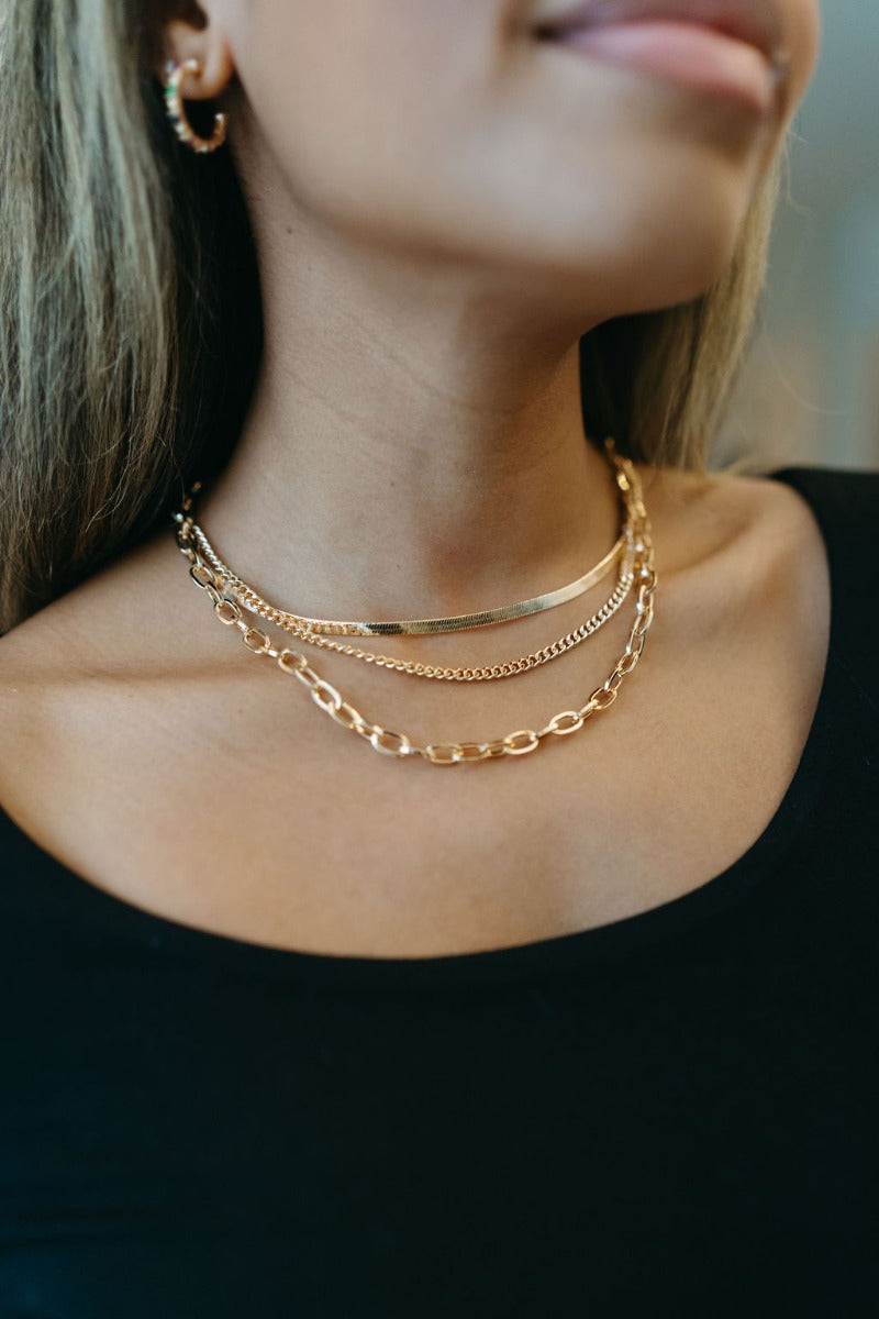 Close up view of model wearing the Love Endlessly Triple Layer Necklace which features triple layer with gold chain links and flat layer.